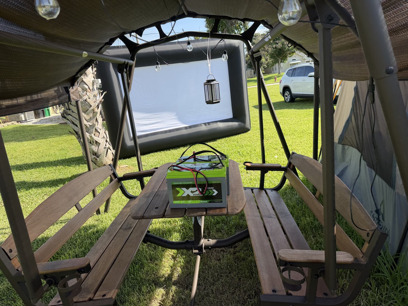 Camp No Pants lot with picnic swing, power batteries, string lights, and giant inflatable movie screen